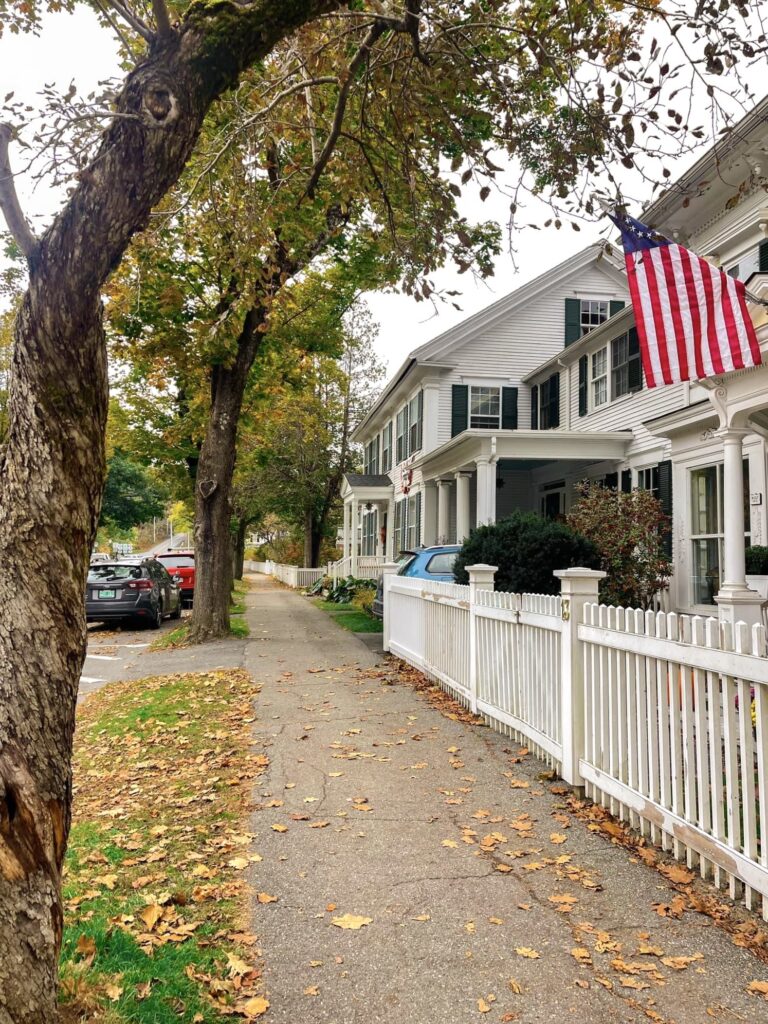 street in downtown Stockbridge, Massachusetts with sidewalk, trees, white picket fence, and flag