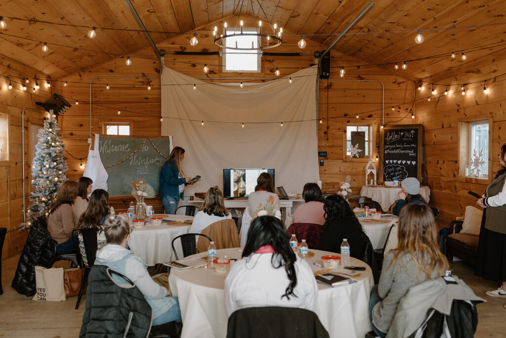 Group of business owners sitting at tables with white tablecloths while someone speaks at the front of the room