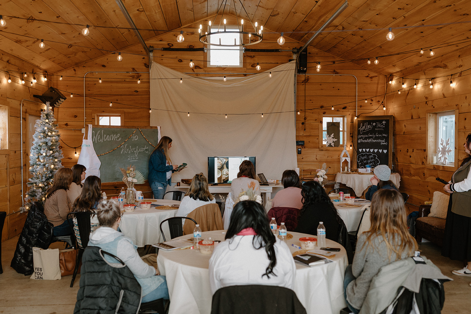 Group of business owners sitting at tables with white tablecloths while someone speaks at the front of the room