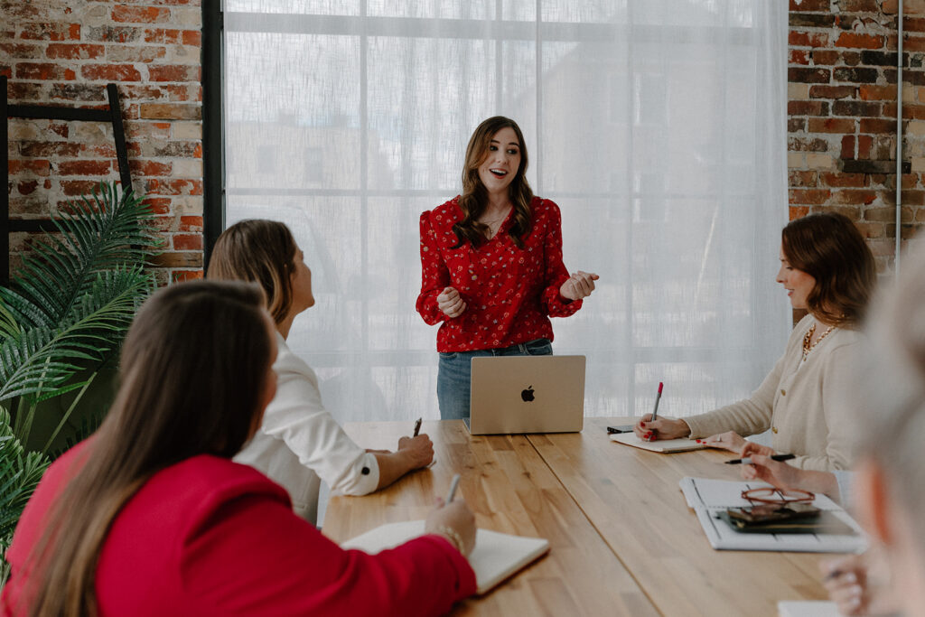 Woman talking with her hands with a laptop open and people around a conference table listening