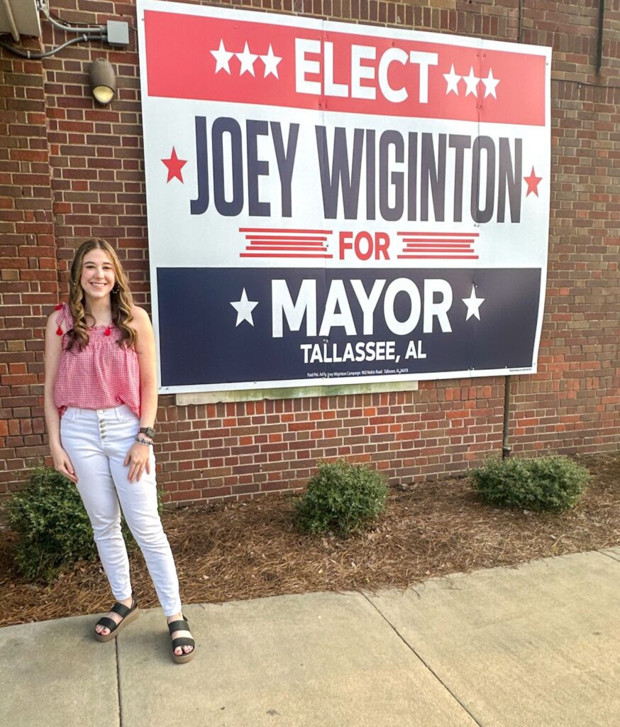 Madelyn Furlong standing in front of a mayoral campaign sign on election night after running social media for political campaigns